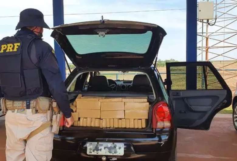 Policial diante dos tabletes de maconha encontrados no porta-malas do veículo. - Crédito: Divulgação PRF 